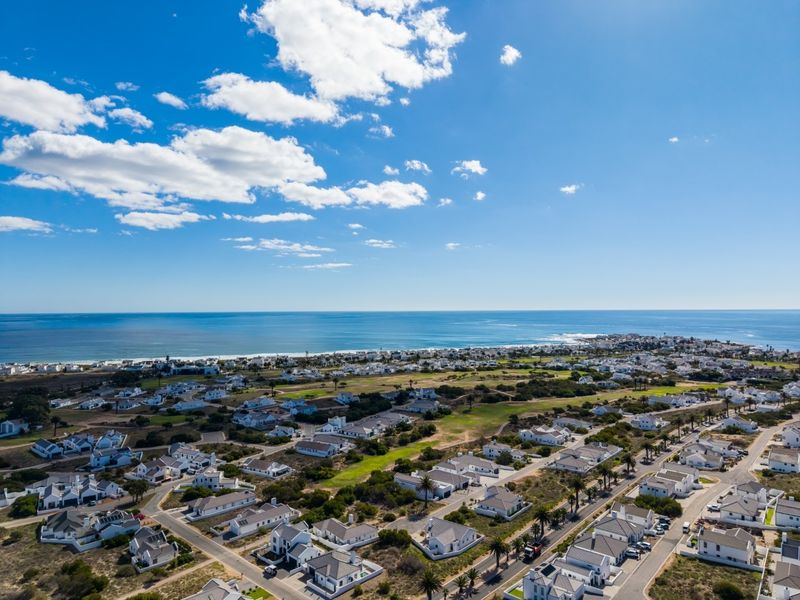 An elevated aerial view of a coastal residential estate, showcasing the surrounding landscape, proximity to the ocean, and neighborhood layout.
