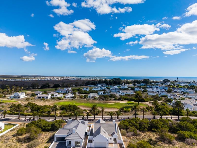 An aerial view of a coastal residential estate featuring well-maintained homes, a golf course, and scenic ocean views.