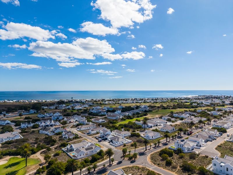 An aerial view of a coastal residential estate featuring well-maintained homes, paved streets, and proximity to the ocean.