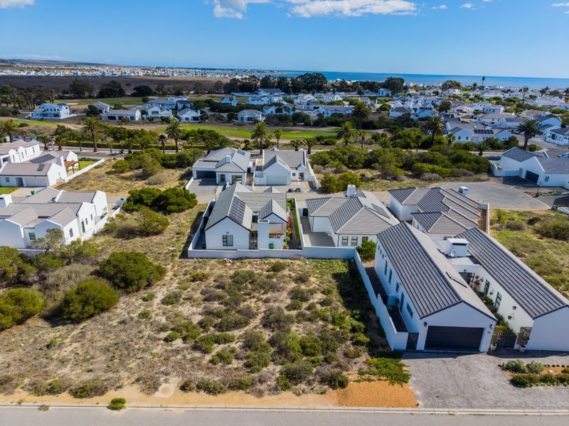 An aerial view of a residential estate featuring modern homes, paved streets, and surrounding coastal landscape.
