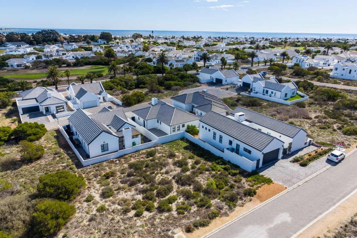 Aerial view of a modern residential estate featuring white homes with dark tiled roofs, paved driveways, and coastal landscape surroundings.
