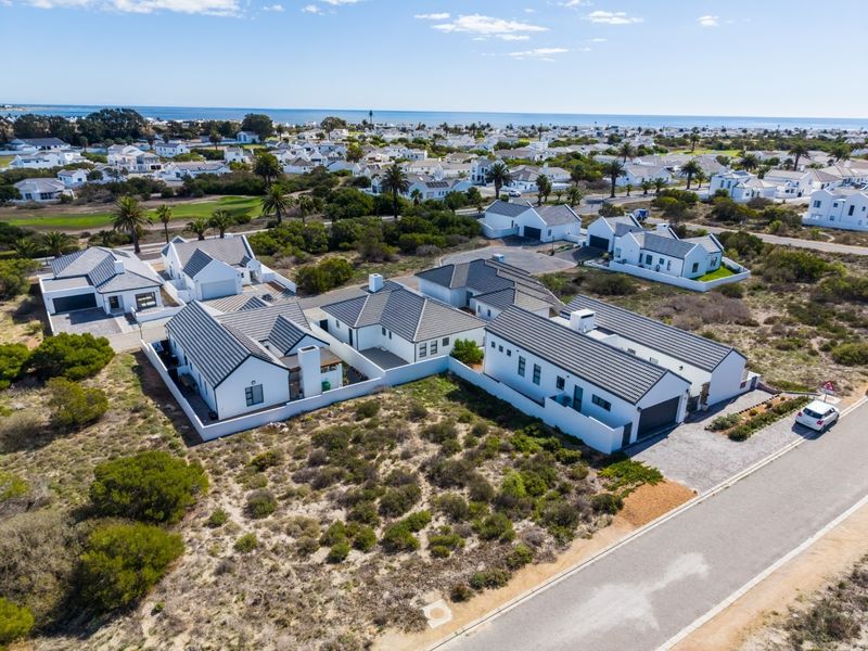 Aerial view of a modern residential estate featuring white homes with dark tiled roofs, paved driveways, and coastal landscape surroundings.