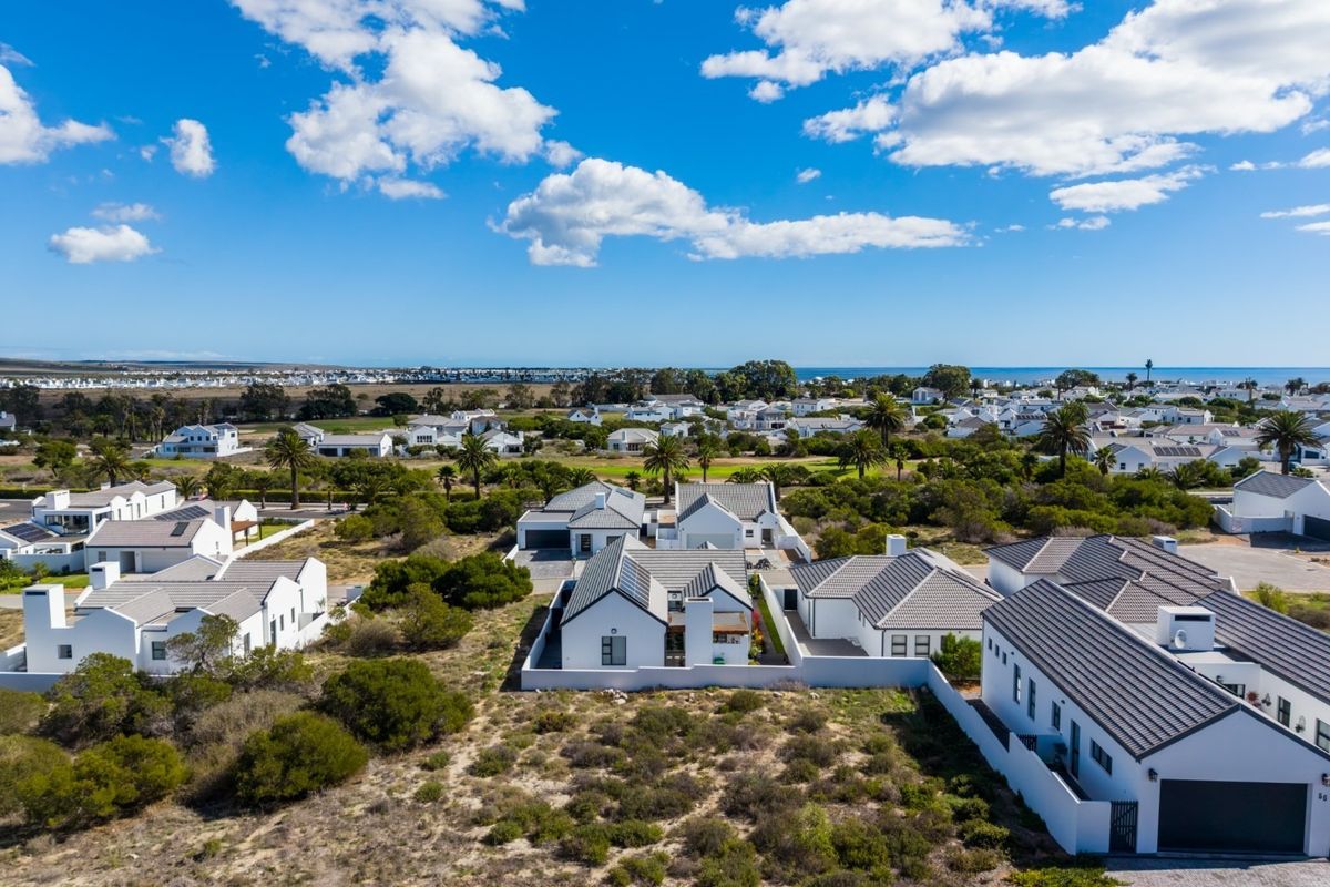 Aerial view of a modern residential estate featuring white houses with tiled roofs, surrounded by coastal landscape and vegetation.