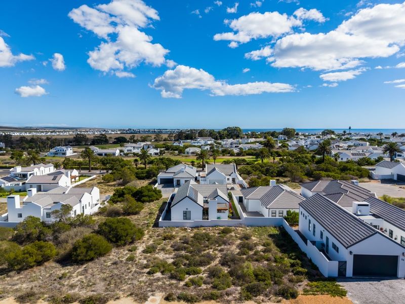 Aerial view of a modern residential estate featuring white houses with tiled roofs, surrounded by coastal landscape and vegetation.