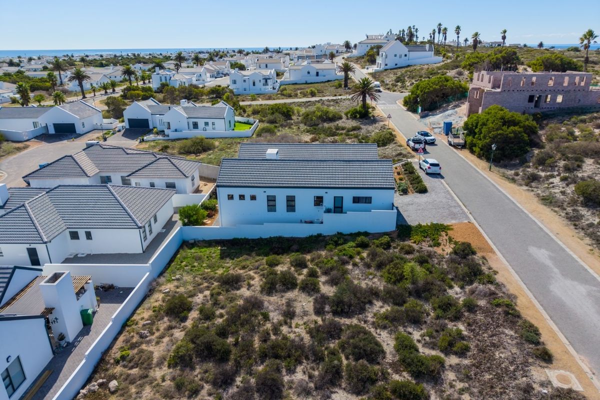 Aerial view of a residential plot in a coastal estate, showcasing the surrounding neighborhood, road access, and existing property infrastructure.
