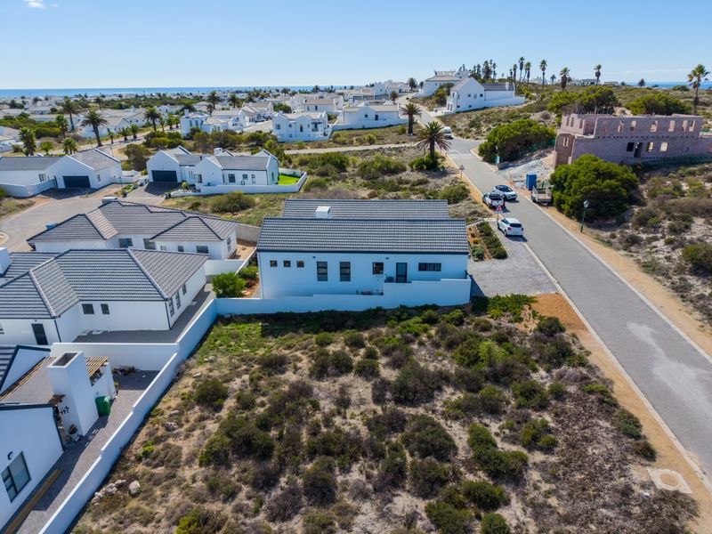 Aerial view of a residential plot in a coastal estate, showcasing the surrounding neighborhood, road access, and existing property infrastructure.