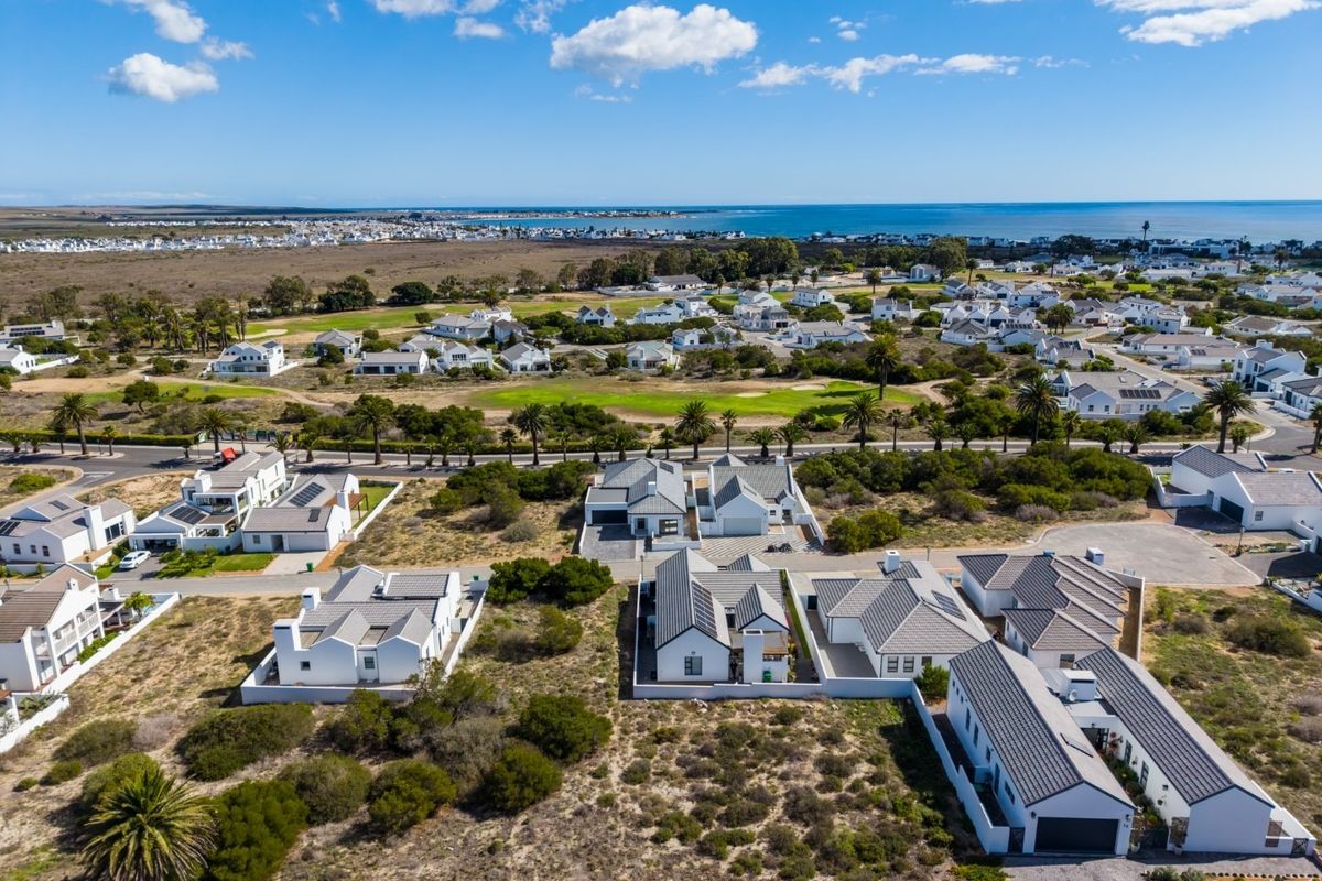 An aerial view of a residential estate featuring modern homes, paved infrastructure, and surrounding coastal landscape with clear ocean views.