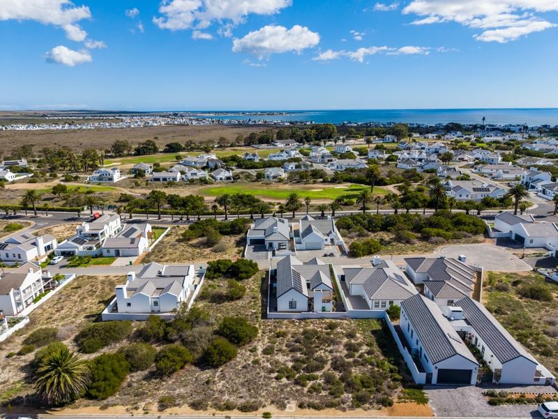 An aerial view of a residential estate featuring modern homes, paved infrastructure, and surrounding coastal landscape with clear ocean views.