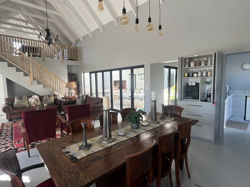 Spacious open-plan living and dining area featuring a double-volume vaulted ceiling, exposed rafters, timber staircase, and seamless access to the outdoor patio through bi-fold doors.