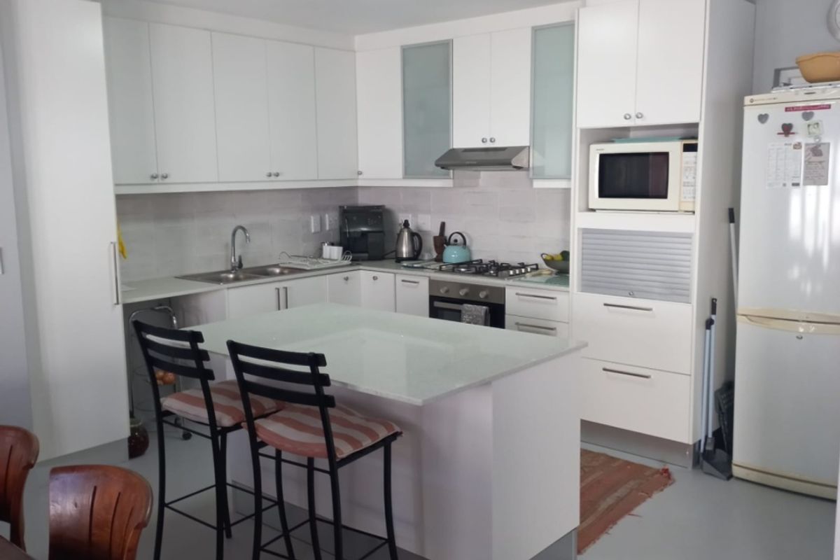 Modern kitchen featuring white cabinetry, a central island with breakfast bar seating, integrated appliances, and a gas hob with extractor fan.