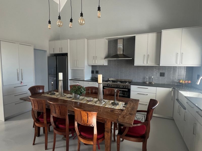 Spacious open-plan kitchen and dining area featuring modern white cabinetry, a gas stove with extractor, tiled backsplash, and a farmhouse-style apron sink.