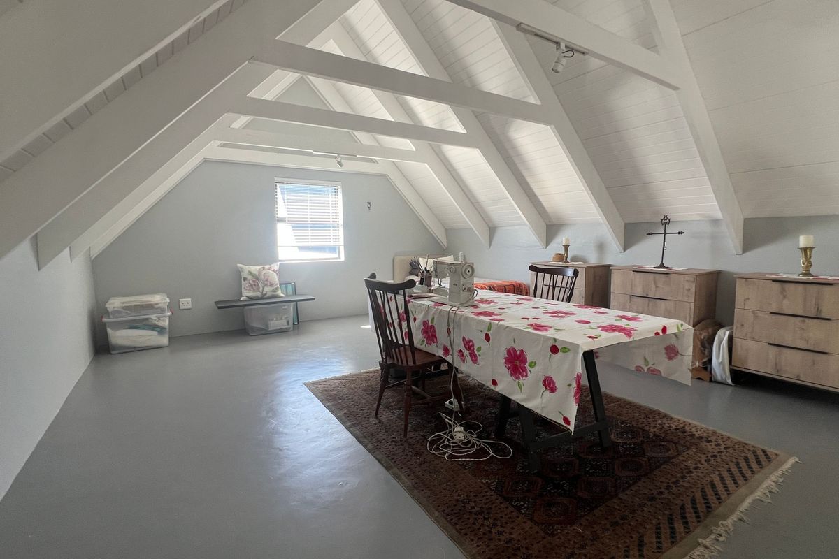 Spacious attic-style bedroom featuring a pitched ceiling with exposed white timber rafters and smooth painted concrete flooring.