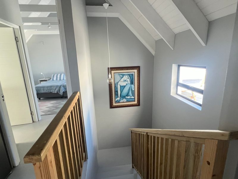 A bright hallway featuring exposed rafter ceilings, a timber balustrade, and a view into an adjacent bedroom.