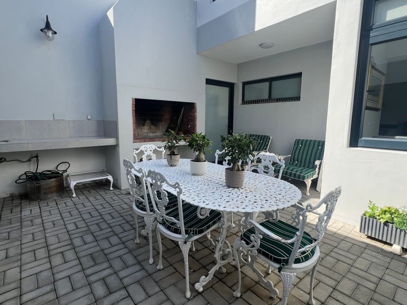Covered patio area featuring a built-in braai, concrete prep counter with sink, and paved flooring, ideal for outdoor entertaining.