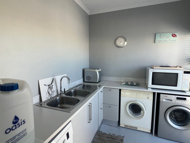 A functional laundry room featuring built-in cabinetry, a double stainless steel sink, and integrated laundry appliances.