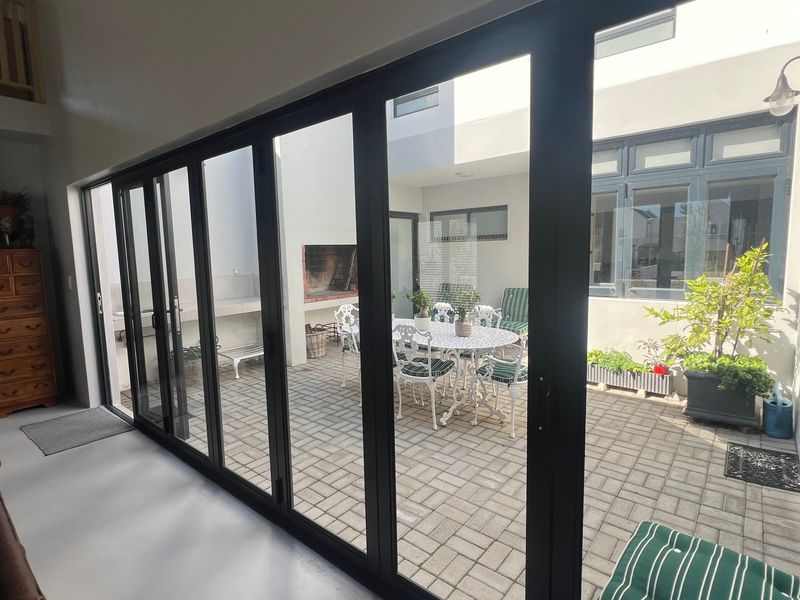 A covered patio area featuring large stacking glass doors, paved flooring, and a built-in braai, seamlessly connecting the indoor and outdoor living spaces.
