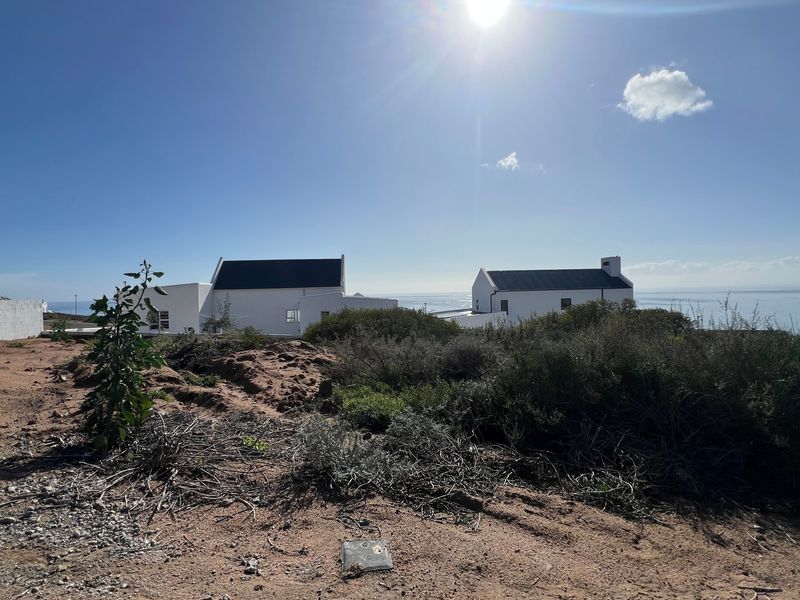 A view of the vacant residential land with coastal scenery and neighboring properties in the distance.