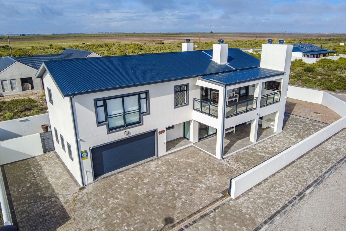 Aerial view of a modern two-story house featuring a metal roof, paved driveway, integrated garage, and an upper-level balcony with glass balustrades.