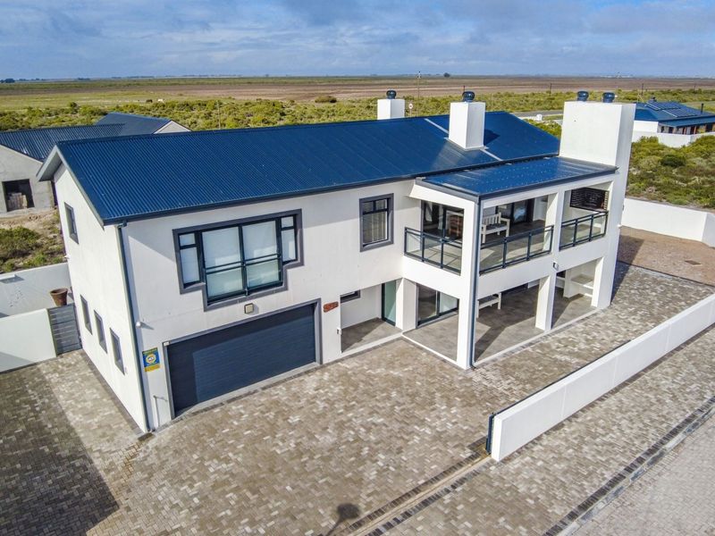 Aerial view of a modern two-story house featuring a metal roof, paved driveway, integrated garage, and an upper-level balcony with glass balustrades.