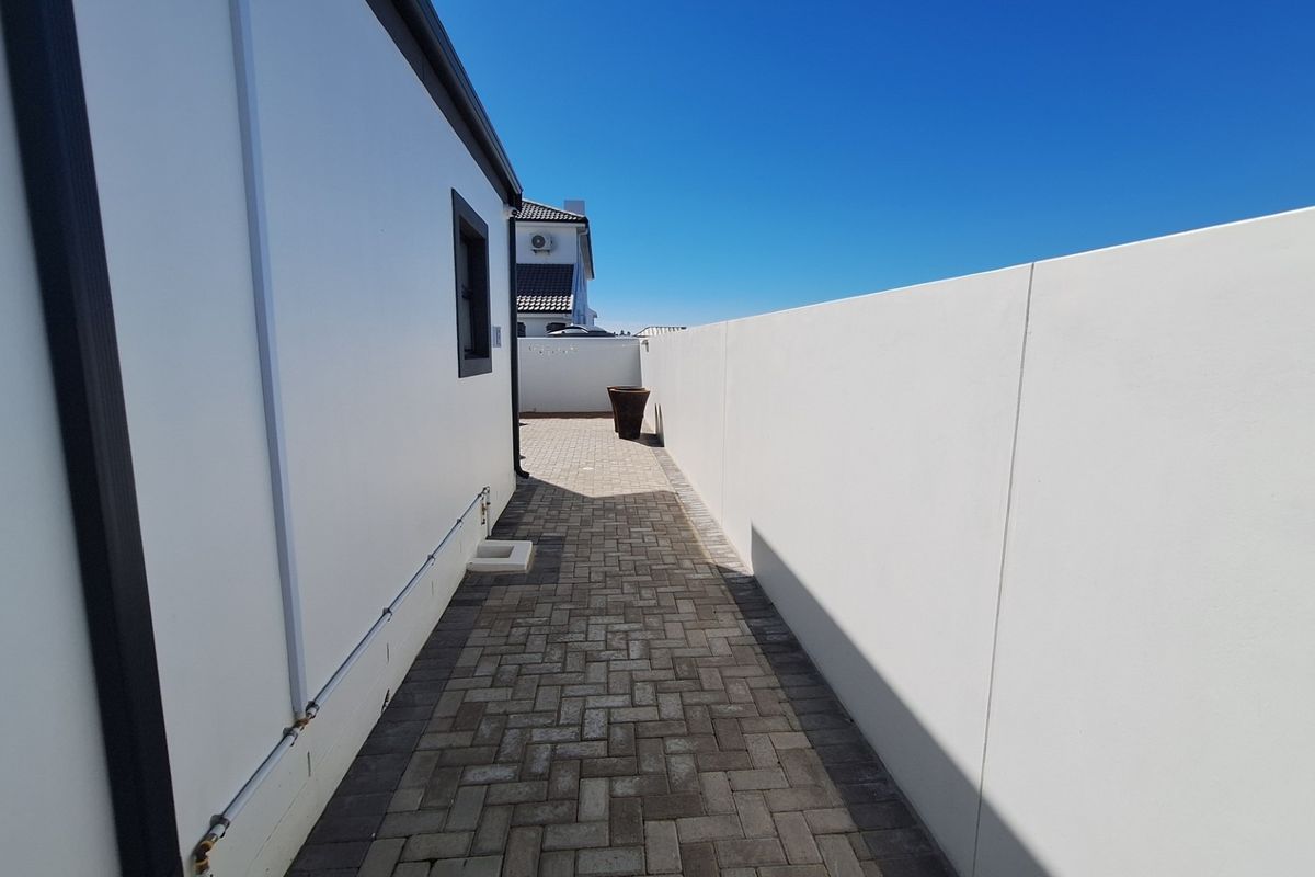 A clean, paved side walkway featuring a high boundary wall and well-maintained exterior finishes.