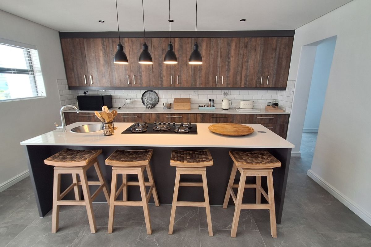 Modern kitchen featuring a central island with a gas cooktop, stone countertops, subway tile backsplash, and dark wood-finish cabinetry.