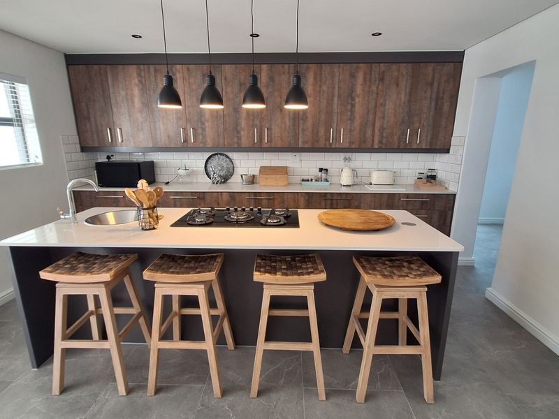 Modern kitchen featuring a central island with a gas cooktop, stone countertops, subway tile backsplash, and dark wood-finish cabinetry.
