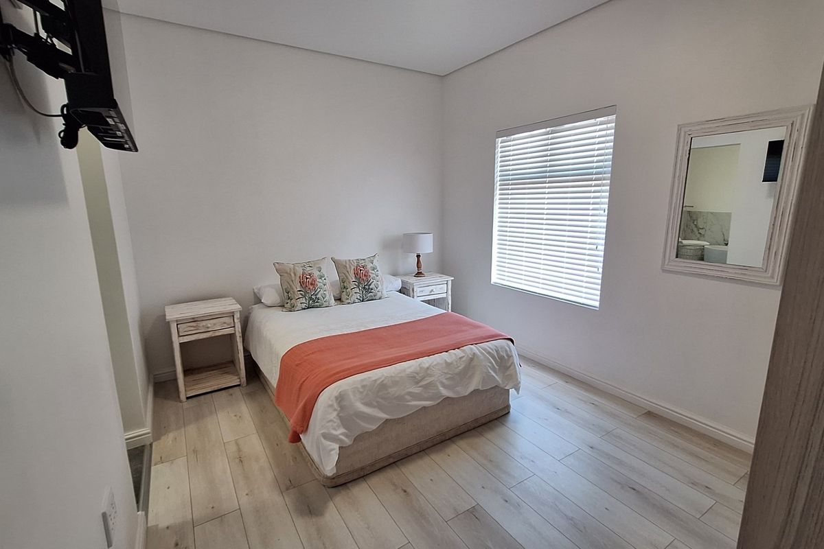 A well-maintained bedroom featuring light-toned laminate flooring, neutral walls, and fitted venetian blinds, offering a clean and comfortable living space.