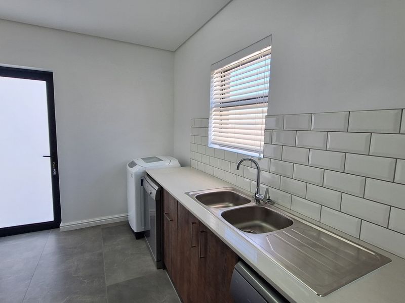 A clean and functional scullery featuring a double stainless steel sink, subway tile backsplash, modern cabinetry, and direct access to the exterior.