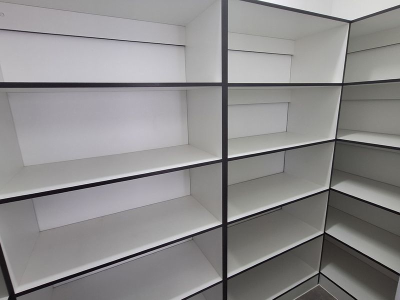 A clean, empty walk-in pantry or scullery featuring extensive built-in white shelving with dark trim.