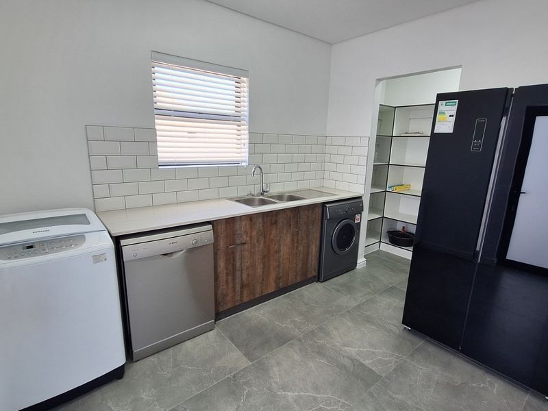 Modern scullery featuring stone countertops, subway tile backsplash, stainless steel sink, and an adjoining walk-in pantry with ample storage space.