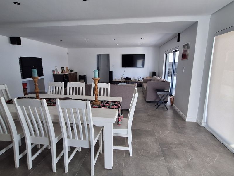 Spacious open-plan living and dining area featuring large format floor tiles, recessed lighting, and seamless access to the outdoor patio through sliding glass doors.