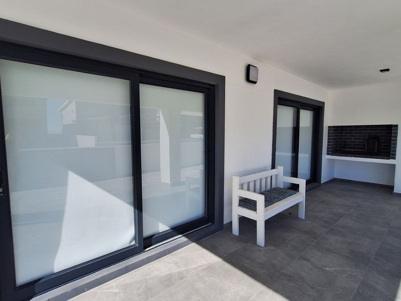 A modern covered patio featuring large sliding glass doors, tiled flooring, and a built-in braai area, perfect for outdoor entertaining.