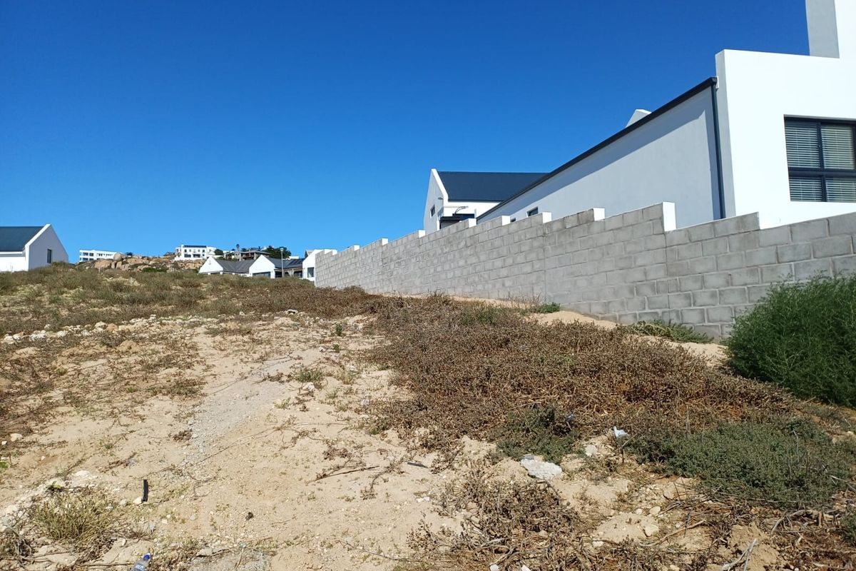 Vacant residential land plot featuring a concrete block boundary wall and views of the surrounding coastal estate neighborhood.