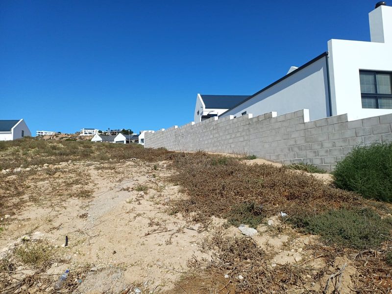 Vacant residential land plot featuring a concrete block boundary wall and views of the surrounding coastal estate neighborhood.