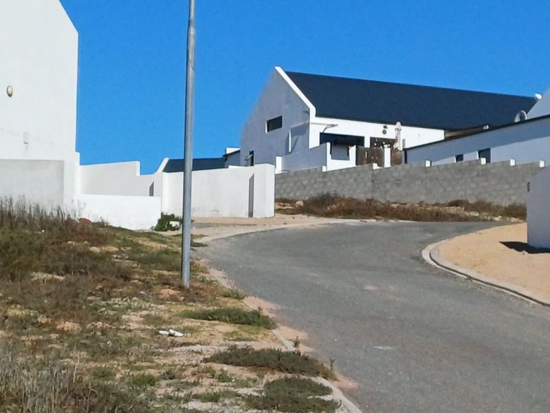 A street view showing the asphalt road, surrounding residential properties, and boundary walls in a developing residential area.