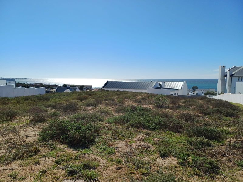 A vacant residential plot offering expansive ocean views, situated in a coastal neighborhood with surrounding established properties.
