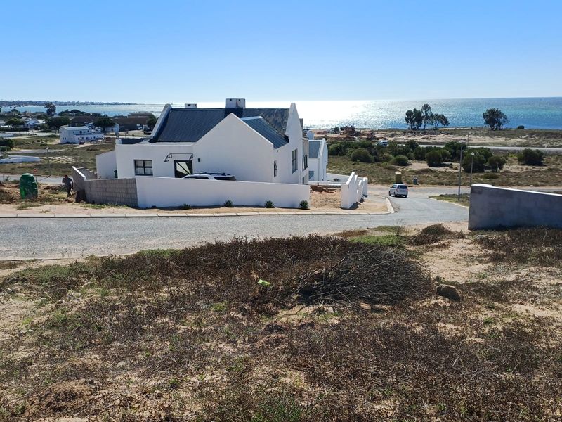 A view of a residential property with a white facade and metal roof, situated in a coastal area with ocean views.