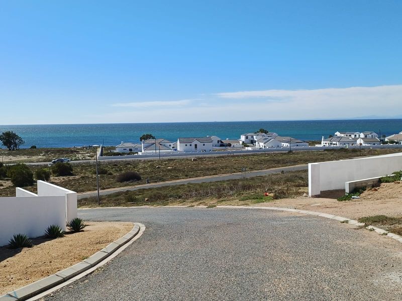 A scenic view overlooking a coastal residential area with paved roads, boundary walls, and a clear ocean horizon.