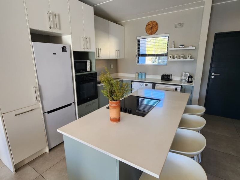 Modern kitchen featuring white cabinetry, a central island with an integrated electric cooktop, tiled flooring, and built-in appliances.