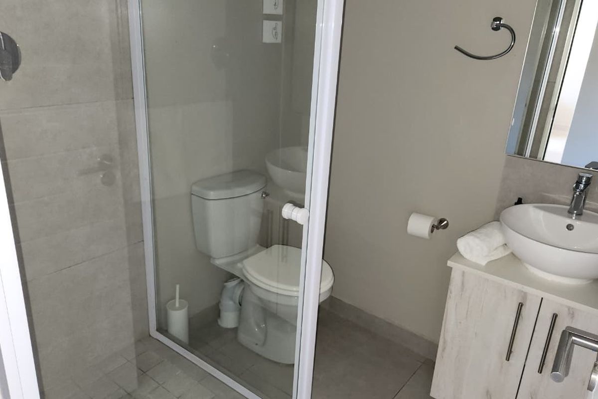 A modern bathroom featuring a glass-enclosed shower, a vanity unit with a vessel sink, and neutral wall and floor tiling.