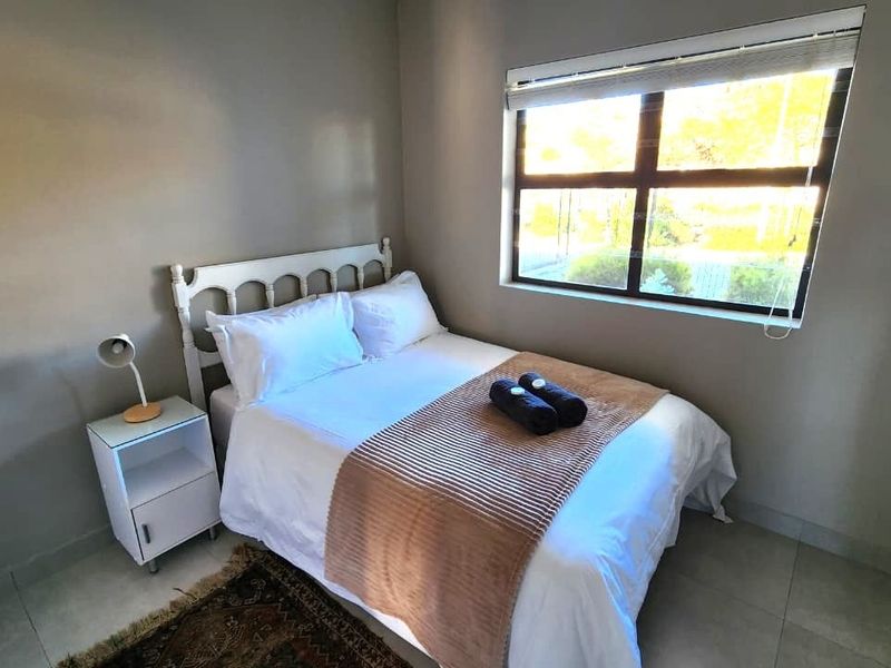 A well-lit bedroom featuring neutral wall tones, tiled flooring, and a large window with fitted blinds.