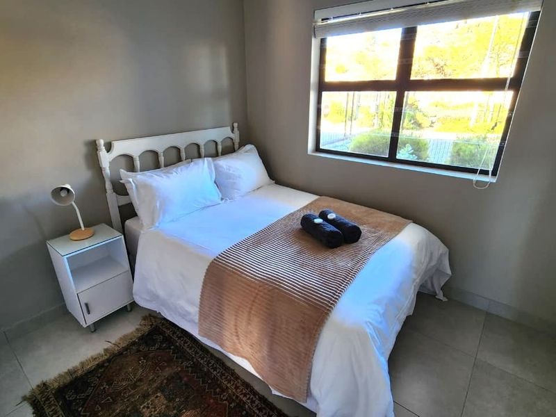 A compact bedroom featuring neutral wall tones, tiled flooring, and a window with fitted blinds, providing a functional and well-lit sleeping space.