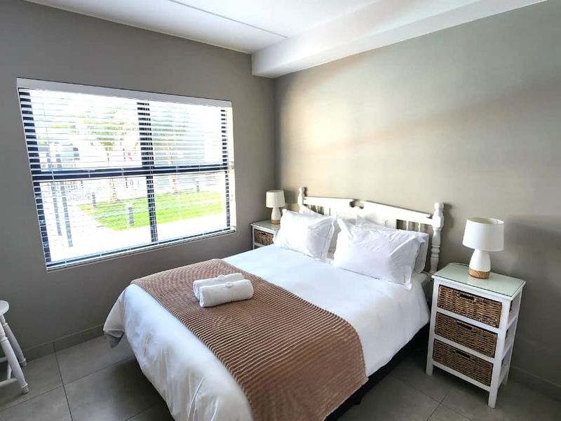 A well-maintained bedroom featuring neutral wall tones, tiled flooring, and a large window with venetian blinds, providing a bright and comfortable living space.
