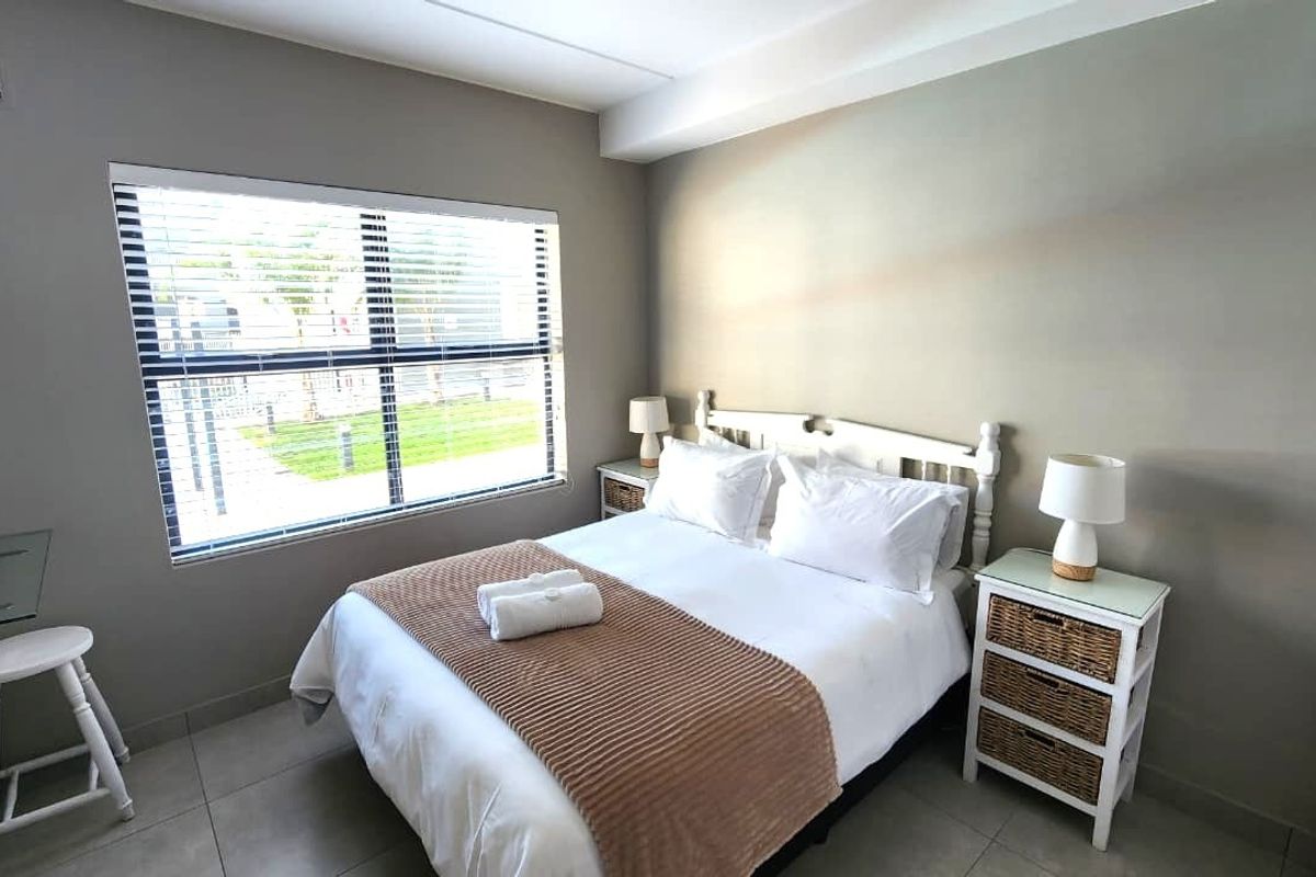 A well-maintained bedroom featuring neutral wall tones, tiled flooring, and a large window with venetian blinds, providing a bright and comfortable living space.