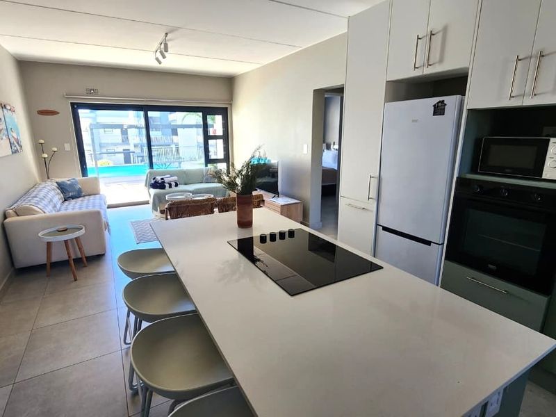 Modern open-plan living area featuring a sleek kitchen with a central island, built-in appliances, and seamless flow to the outdoor patio area.