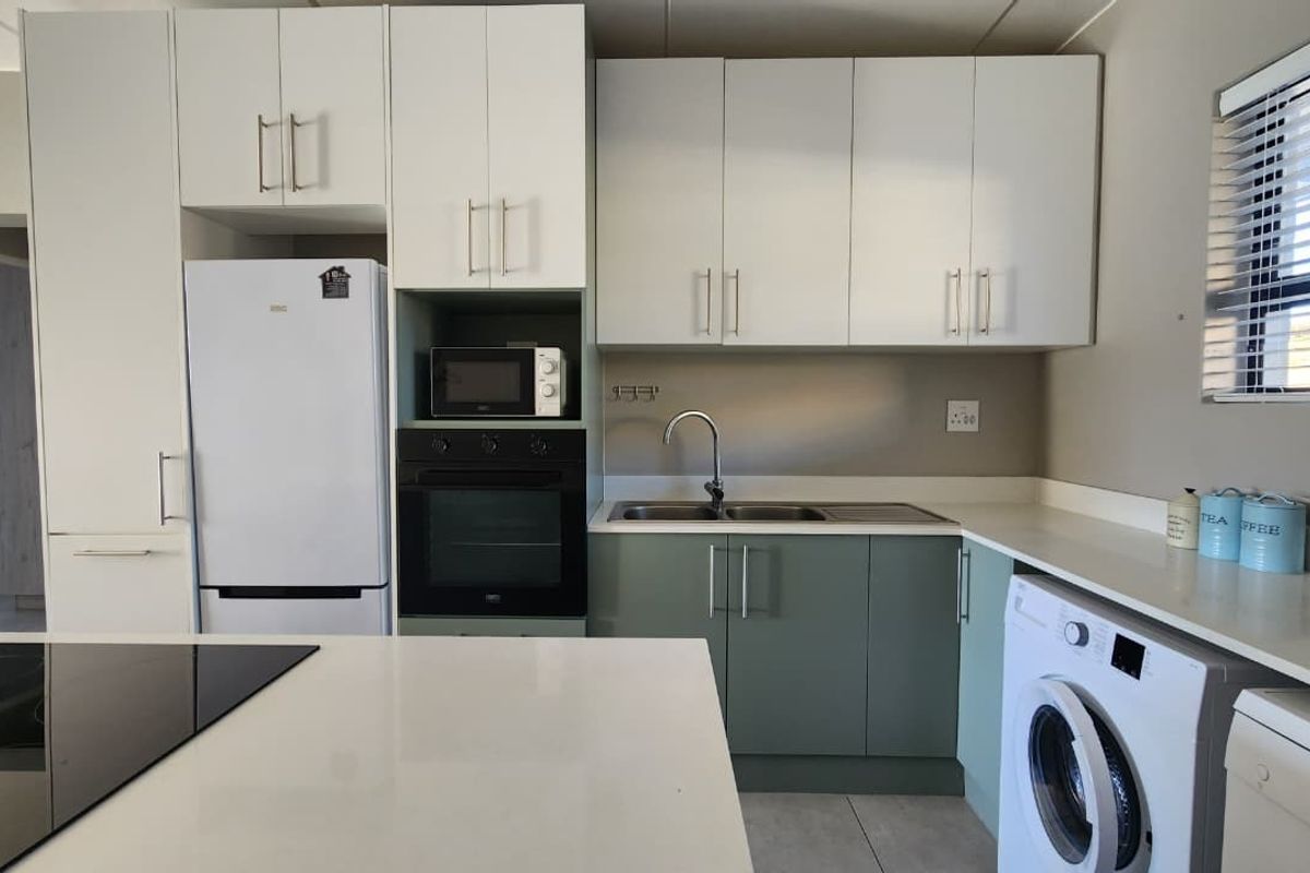 Modern kitchen featuring two-tone cabinetry, stone countertops, built-in oven, hob, and integrated laundry facilities in a clean, functional layout.