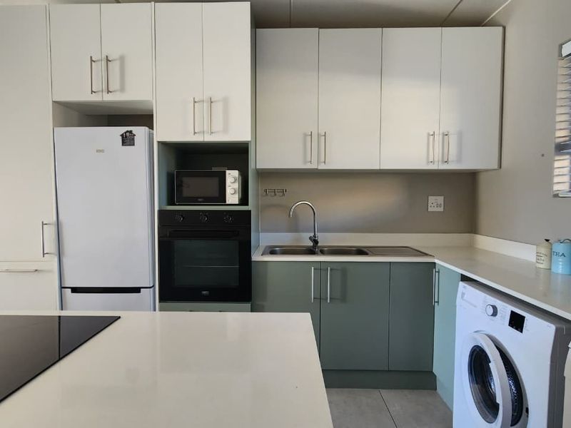 Modern kitchen featuring two-tone cabinetry, stone countertops, built-in oven, hob, and integrated laundry facilities in a clean, functional layout.
