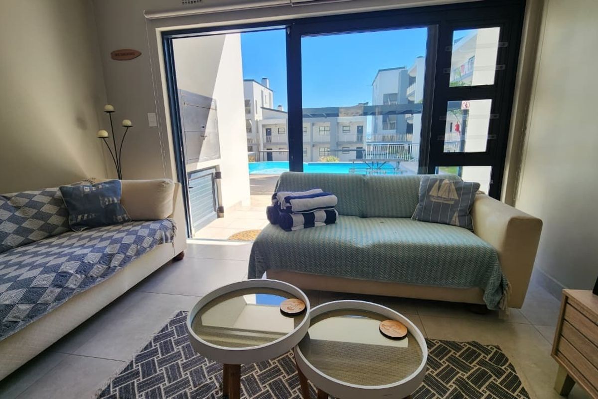 A bright living room featuring large sliding glass doors that open onto a patio area with a view of the swimming pool.