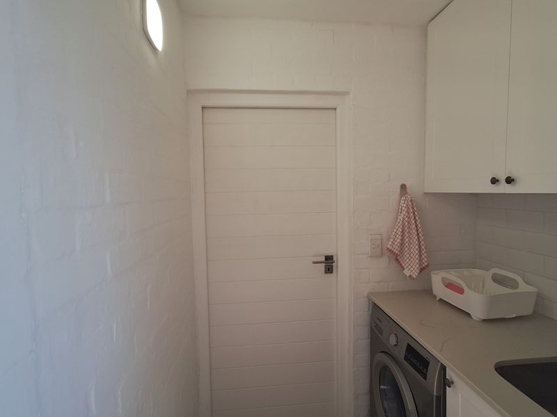 A compact laundry area featuring built-in white cabinetry, a stone countertop, and an integrated sink with washing machine plumbing.