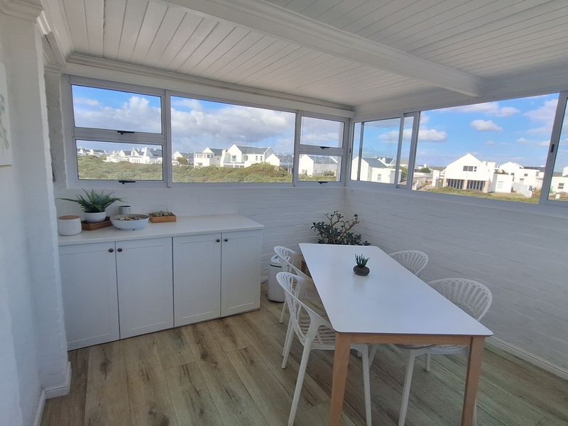 Bright enclosed patio or sunroom featuring built-in cabinetry, large sliding windows with neighborhood views, and modern timber-look flooring.